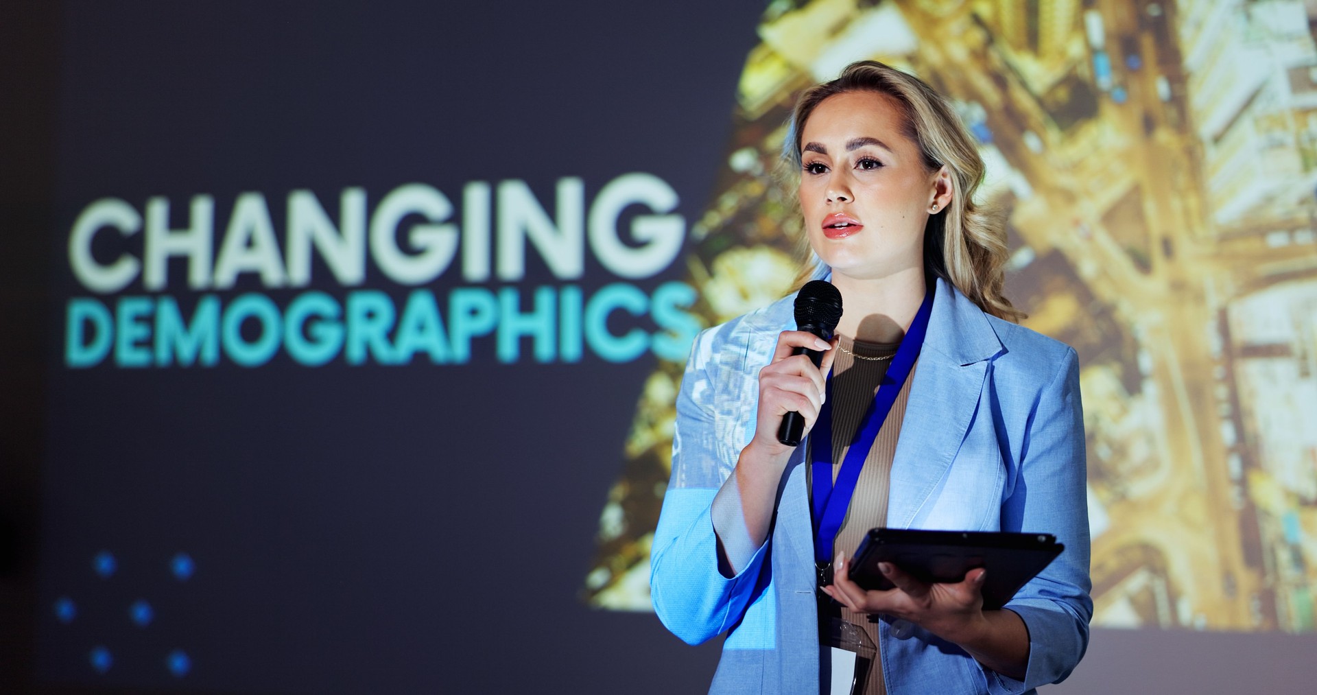 Presenter, conference and woman on a stage with statistics for mortality, population growth and birth or death rate. Public speaking, audience and person on tablet at tradeshow, convention or seminar